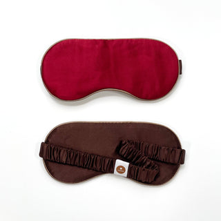 Luxury double-sided silk sleep mask with deep red fabric on one side and rich brown on the reverse, featuring elegant piping and adjustable elastic strap.