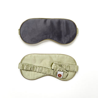 Luxury double-sided silk sleep mask with dark charcoal front and light sage green back, featuring elastic band and quality tag, shown from both sides