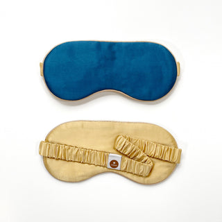 Luxury double-sided silk sleep mask showing rich blue front side above and gold underside with elastic band and brand label below