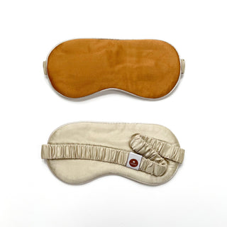 Luxury double-sided silk sleep mask shown from both sides - amber gold top surface and cream silk underside with elastic strap and brand tag
