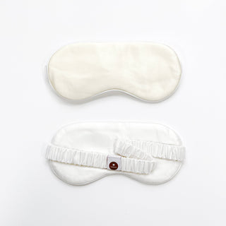Luxury white silk sleep mask shown from front and back, featuring elastic band with brand logo, showcasing smooth satin finish on contoured design