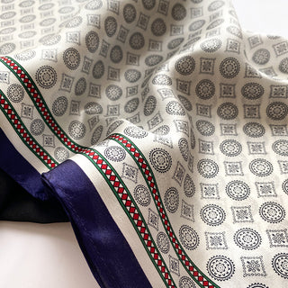 Cream silk neckerchief with decorative medal pattern featuring circular and square motifs, bordered by green and red trim with navy blue edge