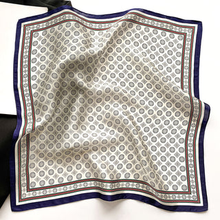 Cream silk neckerchief with geometric medal pattern, navy blue border and red accent trim, displayed flat showing the luxurious texture